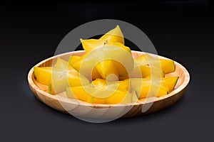 Slice of yellow star fruit on the wooden round tray isolated on black background