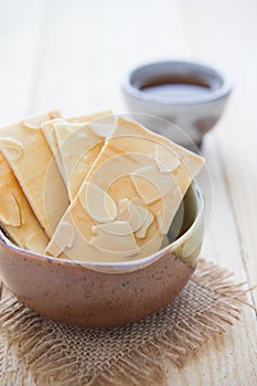 Sliced almond biscuits in the bowl and a cup of hot tea on the w