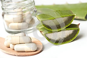 Sliced aloe vera leaves and pills in spoon on white b