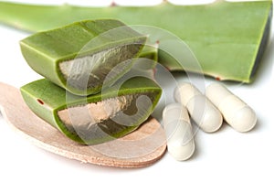 sliced aloe vera leaves and pills in spoon on white background b