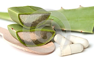 Sliced aloe vera leaves and pills in spoon on white background b