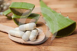 Sliced aloe vera leaves and pills in spoon on wooden
