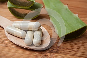 sliced aloe vera leaves and pills in spoon on wooden