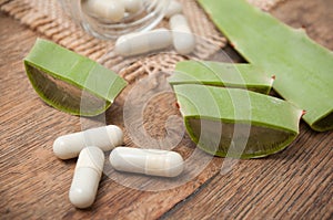 sliced aloe vera leaves and pills on wooden backgroun