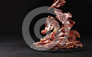 Sliced bacon on black background, raw ham strips