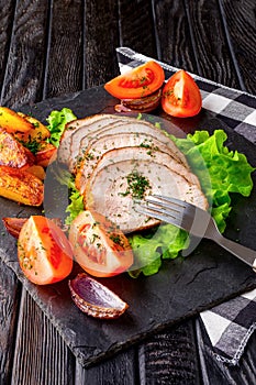 Sliced baked ham with fresh tomatoes on a stone plate in a rustic style