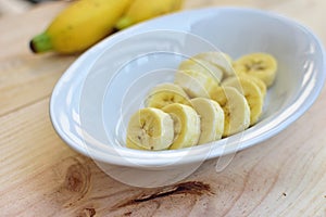 Sliced banana in white bowl on wooden background.