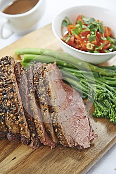 Sliced beef with broccolini and salad on wooden chopping board
