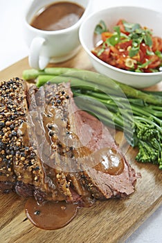 Sliced beef with broccolini and salad on wooden chopping board