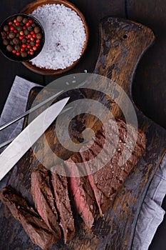 Sliced beef steak with knife and fork and spices on cutting board