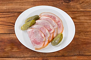 Sliced boiled-smoked pork knuckle and pickled cucumbers on plate