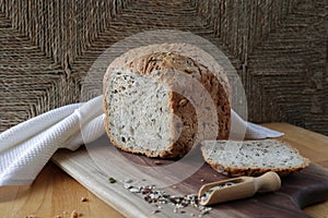 loaf of homemade whole grain bread and a cut slice of bread on a wooden cutting board. Mixture of seeds and whole grains