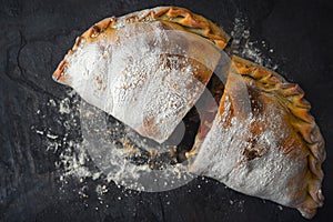 Sliced calzone with flour on the dark stone background top view