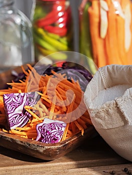 Sliced carrots and red cabbage on a wooden dish. A bag of salt. Harvesting products. Kitchen. Fermented, canned vegetarian food.