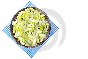 Sliced celery stalk in wooden bowl on paper napkin, white background, top view.