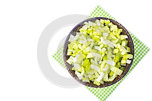 Sliced celery stalk in wooden bowl on paper napkin, white background, top view.