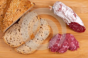 Sliced cereal bread and slices of dried Italian sausage on a wooden cutting board. Simple food for a snack at home. Selective