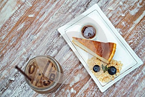 Sliced cheesecake in a white plate is placed near the cold cocoa on the table