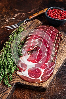 Sliced cured coppa ham on wooden board with thyme. Dark background. Top view