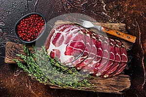 Sliced cured coppa ham on wooden board with thyme. Dark background. Top view