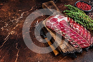 Sliced cured coppa ham on wooden board with thyme. Dark background. Top view. Copy space