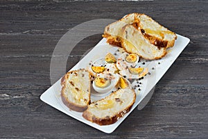 Sliced Easter bread and eggs in white plate on grey wooden board.