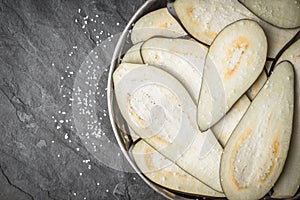 Sliced eggplants with salt in the metal plate on the stone table top view