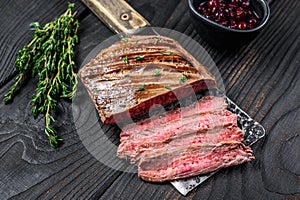 Sliced flank or bavette beef meat steak on a cleaver. Black wooden background. Top view