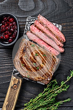 Sliced flank or bavette beef meat steak on a cleaver. Black wooden background. Top view