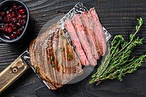 Sliced flank or bavette beef meat steak on a cleaver. Black wooden background. Top view