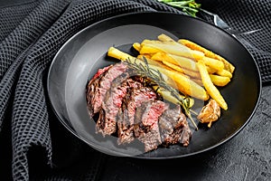 Sliced Flat Iron steak with French fries, marbled meat. Black background. Top view