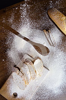 Sliced French baguette on a wooden board  cinnamon sticks and a trail of a large spoon  heavily floured on a wooden table