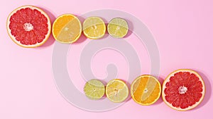 Sliced fresh citrus fruits appear on two sides on pastel pink background with copy space. Stop motion