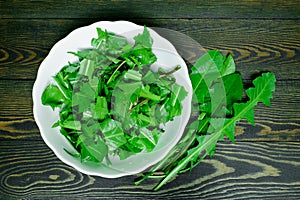 Sliced fresh juicy bright green dandelion leaves in a white plate and several whole leaves on a dark wooden background