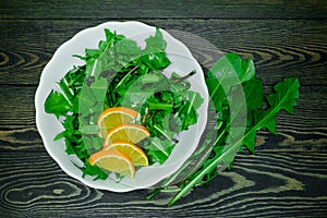 Sliced fresh juicy bright green dandelion leaves in a white plate with slices of lemon and several whole leaves on a dark wooden b