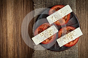 sliced fresh tomatoes under soft cheese with mediterranean spices on a clay plate on a burlap napkin on an old textured wooden
