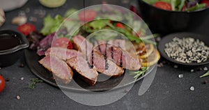 Sliced Fried grilled piece of Organic Tuna Steak on a black ceramic plate with salad