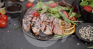 Sliced Fried grilled piece of Organic Tuna Steak on a black ceramic plate with salad