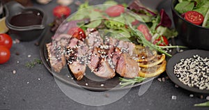 Sliced Fried grilled piece of Organic Tuna Steak on a black ceramic plate with salad