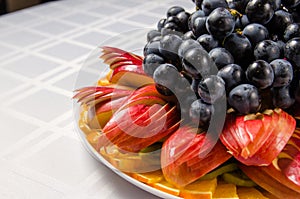 Sliced fruit - apples, oranges, kiwi topped with grapes on white dish