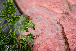 Sliced Grass Fed Juicy Corn Roast Beef garnished with Fresh Curly Parsley on black natural stone