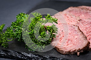 Sliced Grass Fed Juicy Corn Roast Beef garnished with Fresh Curly Parsley on black natural stone