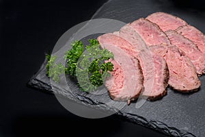 Sliced Grass Fed Juicy Corn Roast Beef garnished with Fresh Curly Parsley on black natural stone