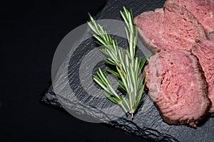 Sliced Grass Fed juicy Corn Roast Beef garnished with Rosemary Fresh Herb on natural black stone