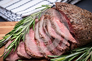 Sliced Grass Fed juicy Corn Roast Beef garnished with Rosemary Fresh Herb on natural wood cutting board