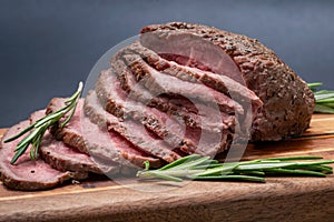 Sliced Grass Fed juicy Corn Roast Beef garnished with Rosemary Fresh Herb on natural wood cutting board
