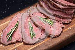 Sliced Grass Fed juicy Corn Roast Beef garnished with Rosemary Fresh Herb on natural wood cutting board