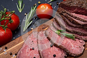 Sliced Grass Fed juicy Corn Roast Beef garnished with Tomatoes, Fresh Rosemary Herb, Garlic and Rainbow Peppercorns