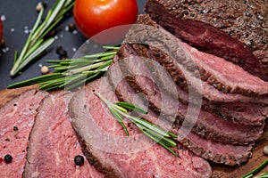 Sliced Grass Fed juicy Corn Roast Beef garnished with Tomatoes, Fresh Rosemary Herb, Garlic and Rainbow Peppercorns