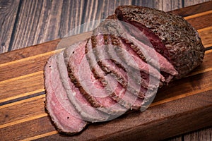 Sliced Grass Fed juicy Corn Roast Beef on wood cutting board.